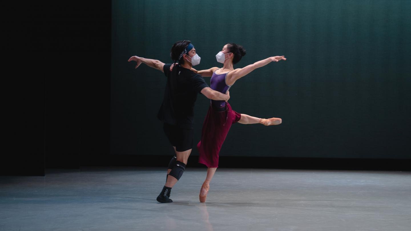 A female dancer stands en pointe as her partner supports her at the waist, they appear to mid-spin