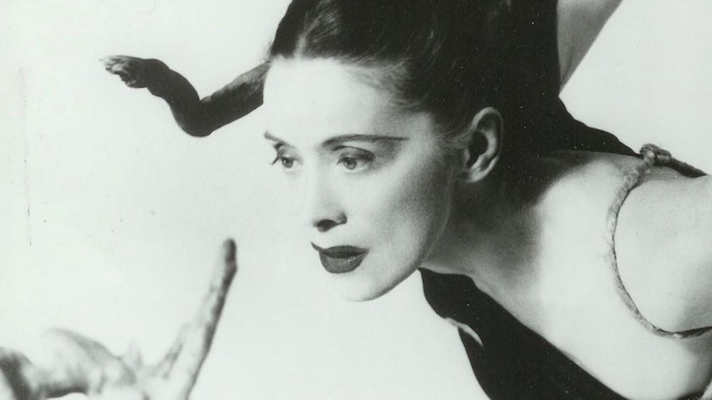 Monochrome image of a woman with bold lipstick leaning forward, her dark hair is tied back and she seems to have rope around her shoulders