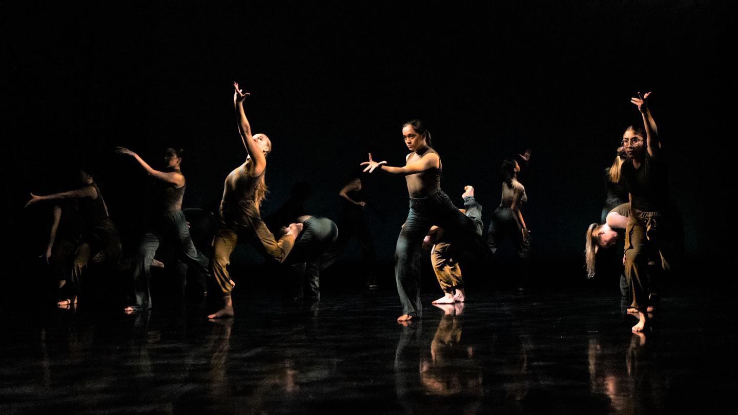 Group of dancers on stage performing against a black background