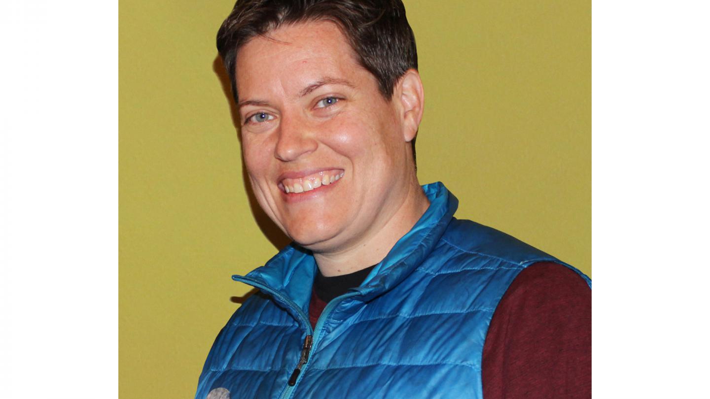 PErson with short, brown hair, wearing a blue life-saver top over a dark red shirt, smiling broadly