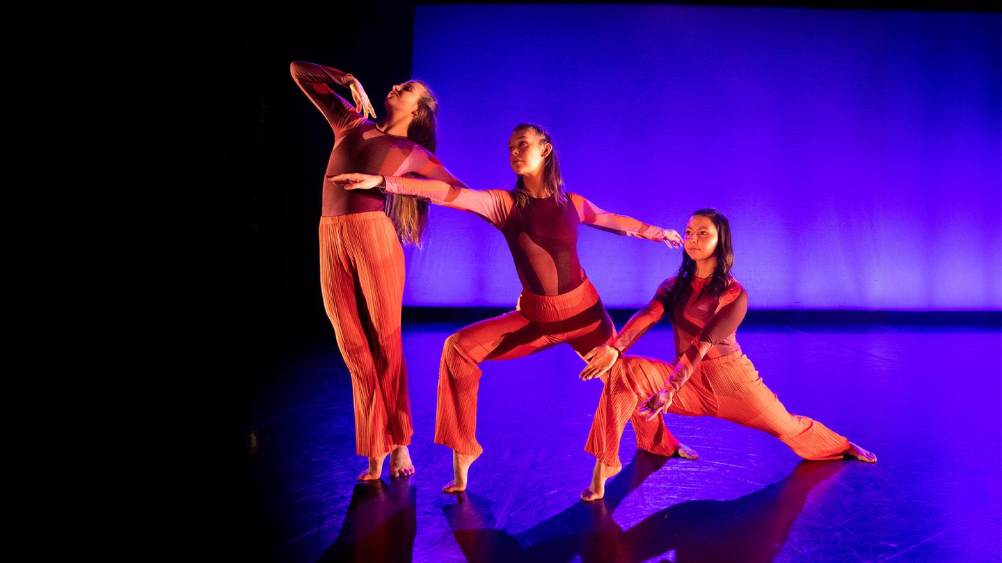 Phoenix Dance Theatre Youth Academy dancers bathed in red light each in a different pose against a blue-lit backdrop