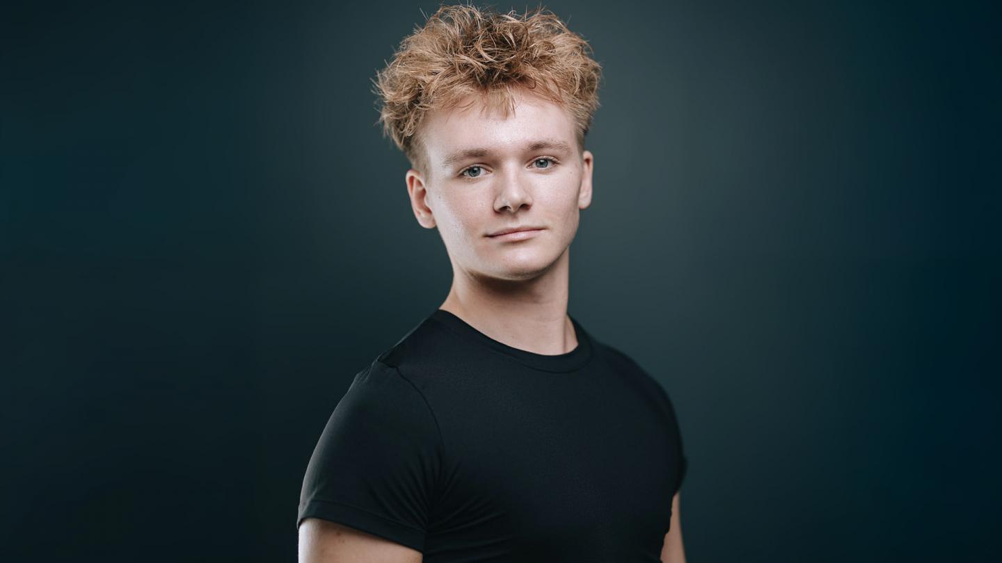 Portrait of shoulders and head of man wearing a black T-shirt, short blond hair and looking directly at the observer