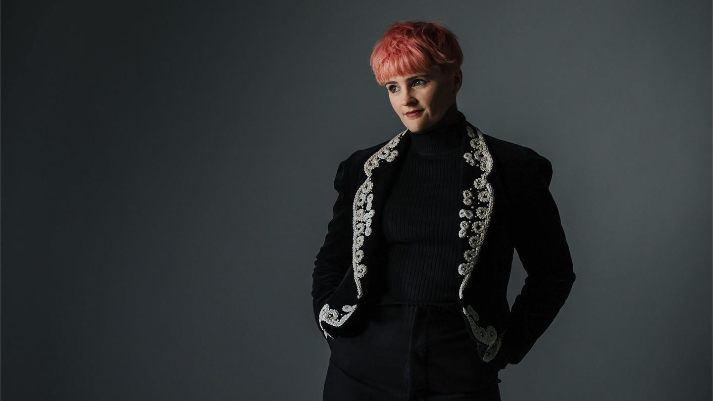 Person in a black jacket with silver trim, and pink hair