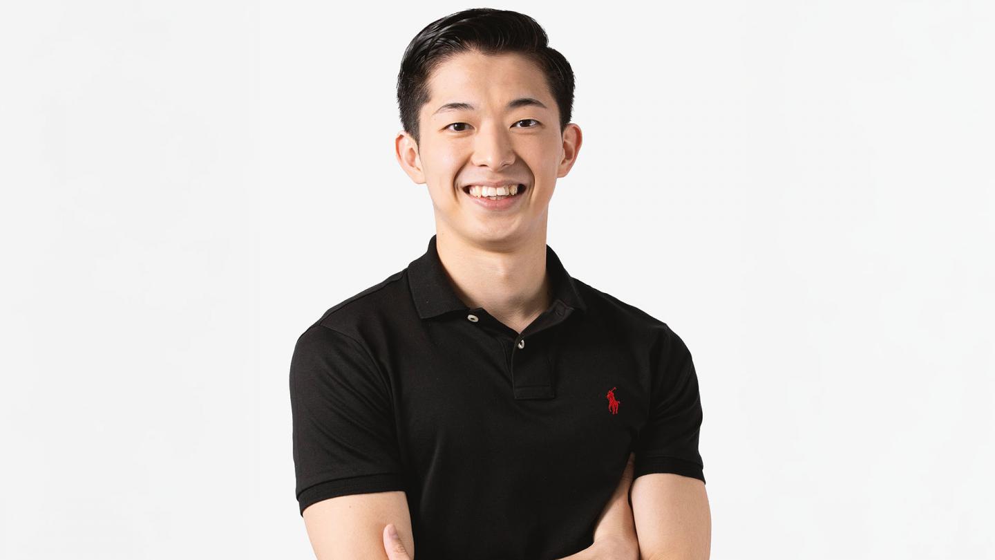 Man in black top with dark hair looking and smiling directly at the camera