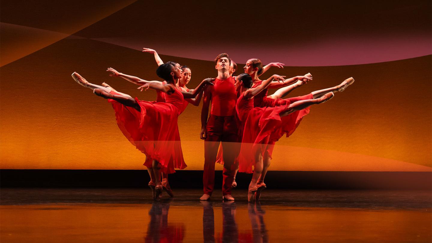 Dancers in red, either side of the central figure people stand arabesque