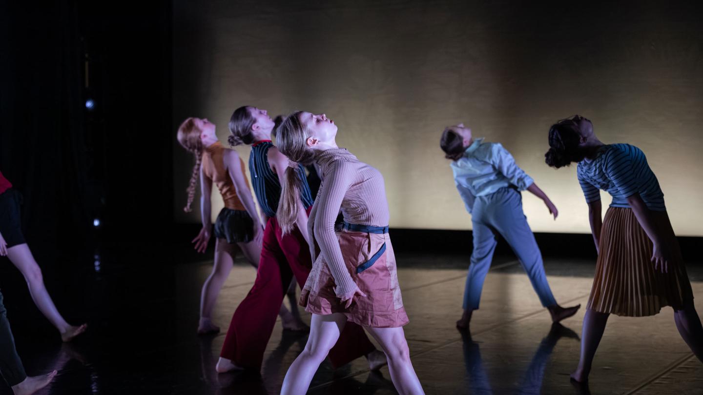 Dancers stepping forward on a stage with their heads leant back. 