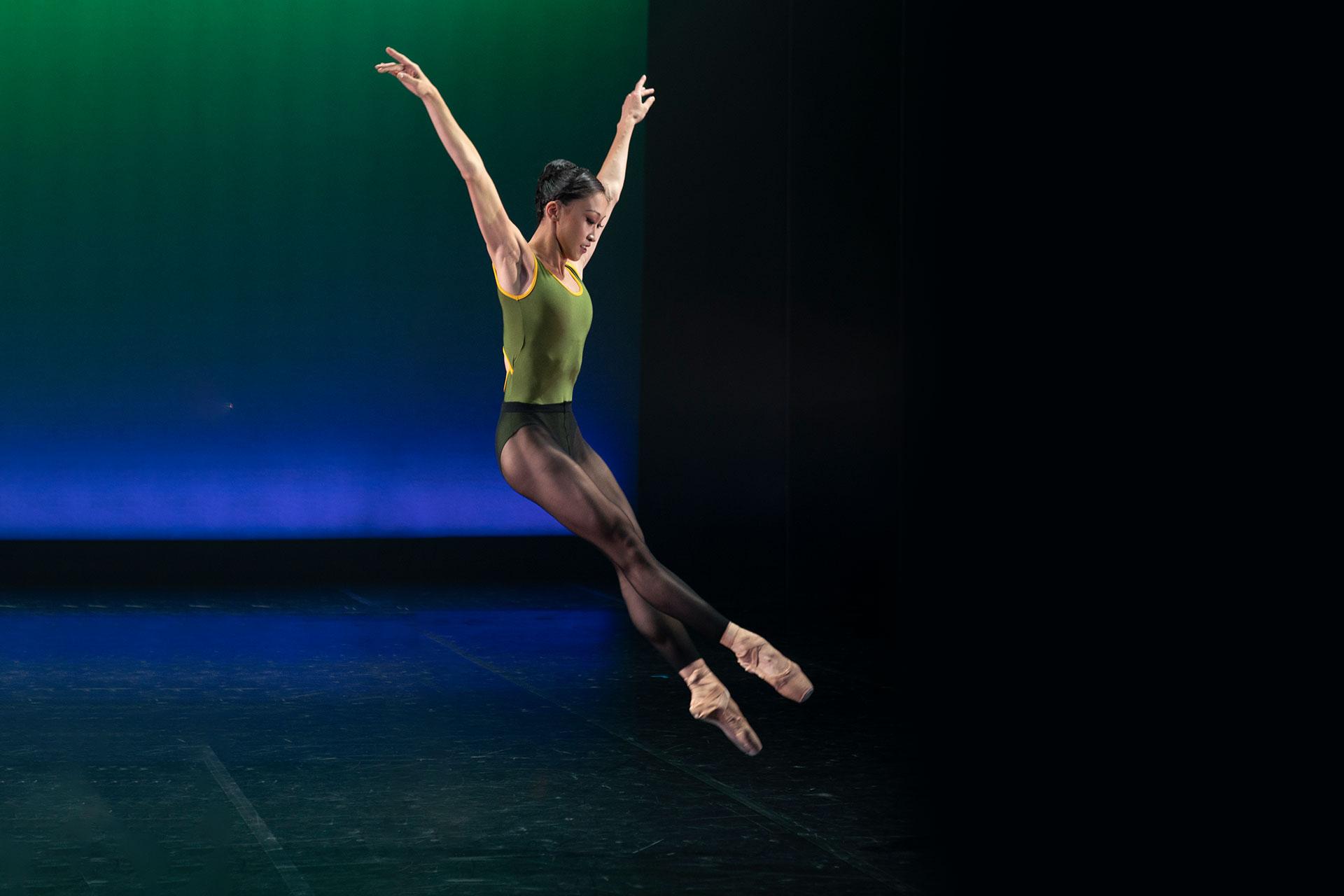 Minju Kang leaping high with her arms above her head and feet pointed perfectly