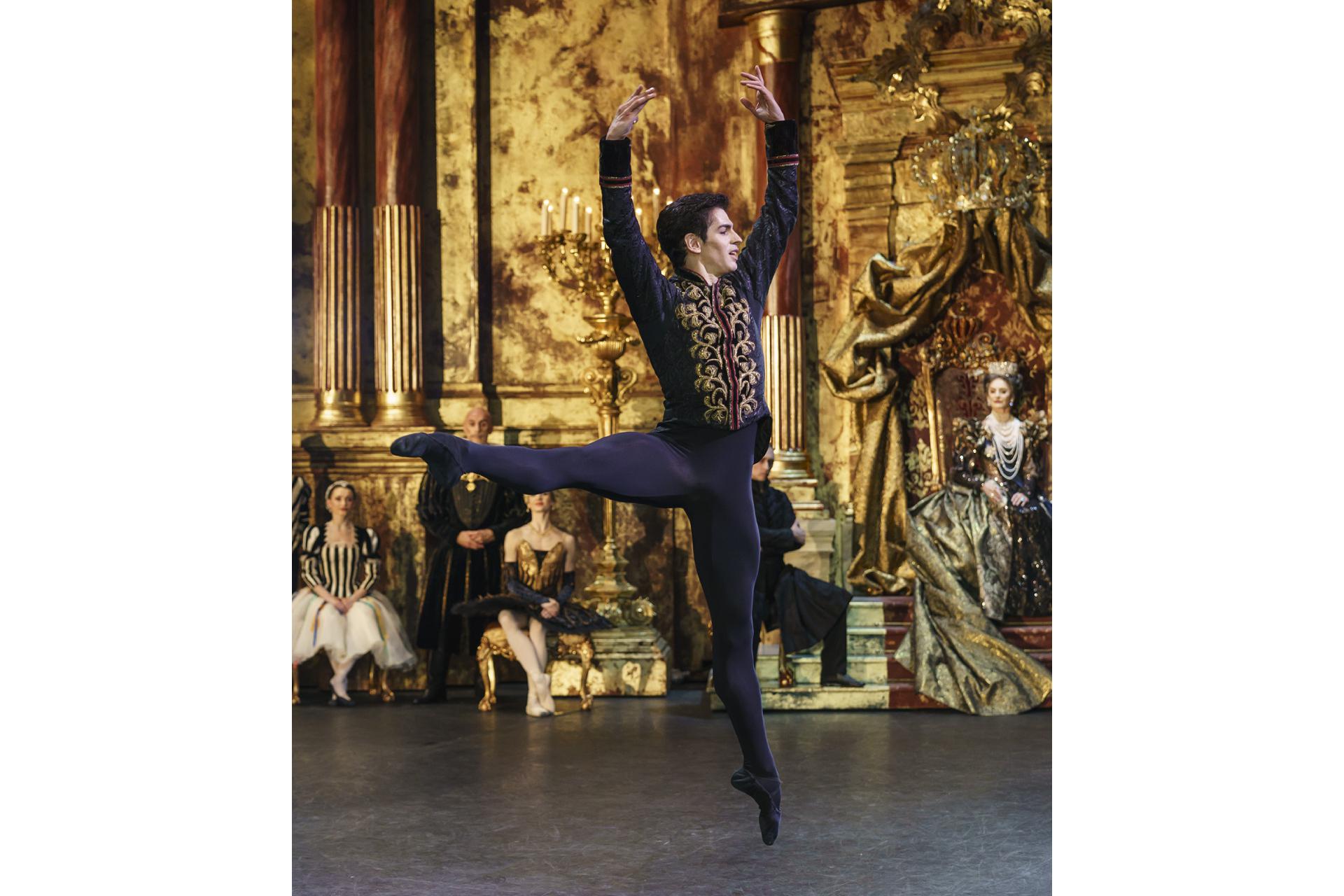 Federico Bonelli leaps in the air, two arms above his head, one foot pointed at the floor and the other foot pointed parallel to the floor.