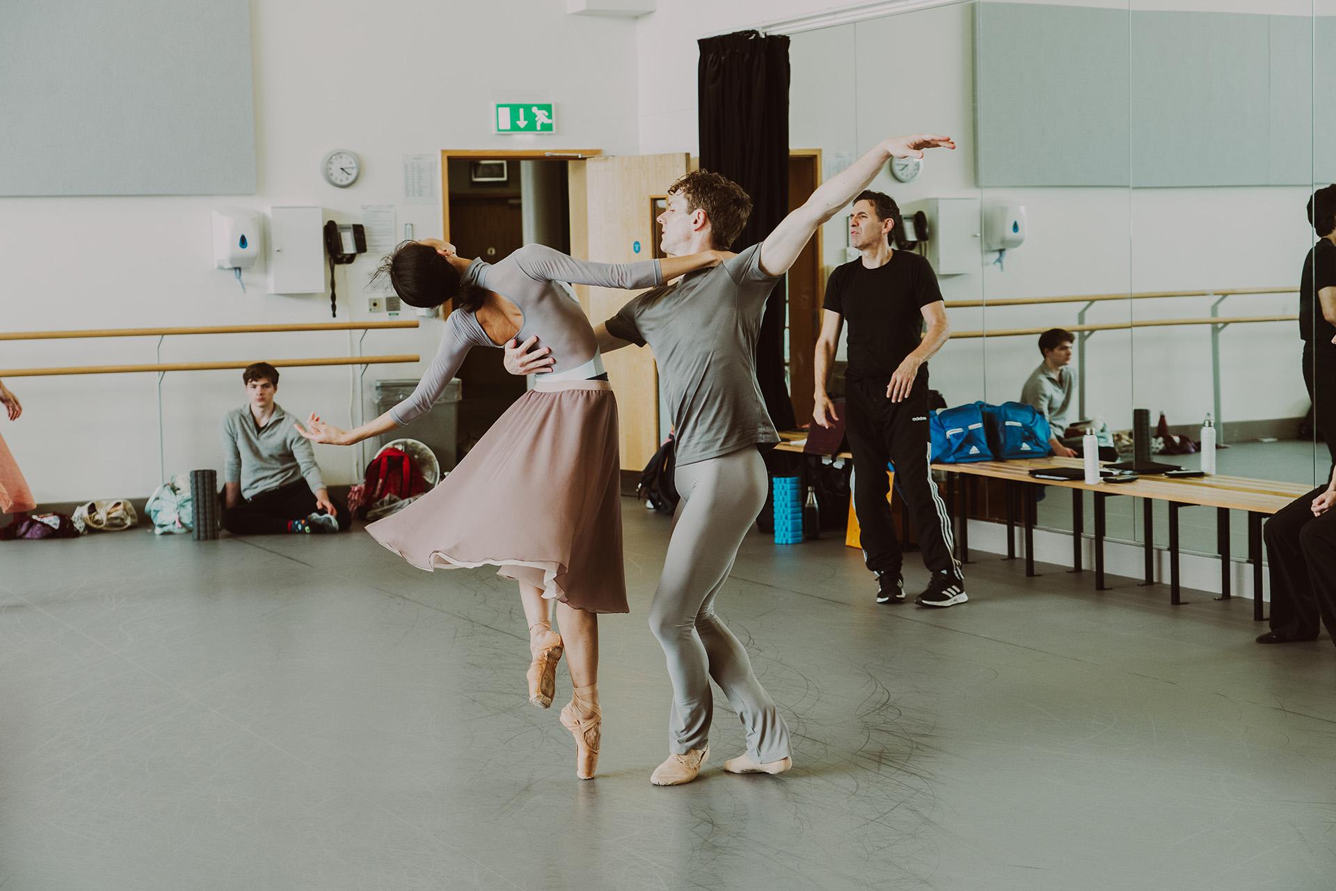 While reaching behind themselves with one arm, Jonathan Hanks and Minju Kang hold on to one another with the other spinning on the spot