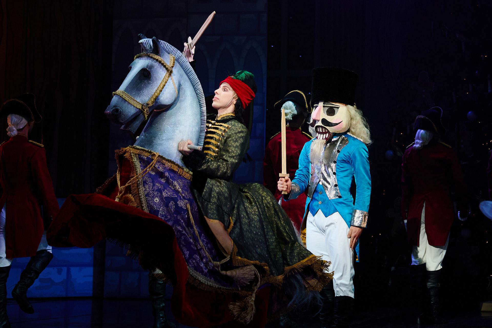 Dancer in military dress rides a fake horse while another wears a papier mache head and holds a wooden sword