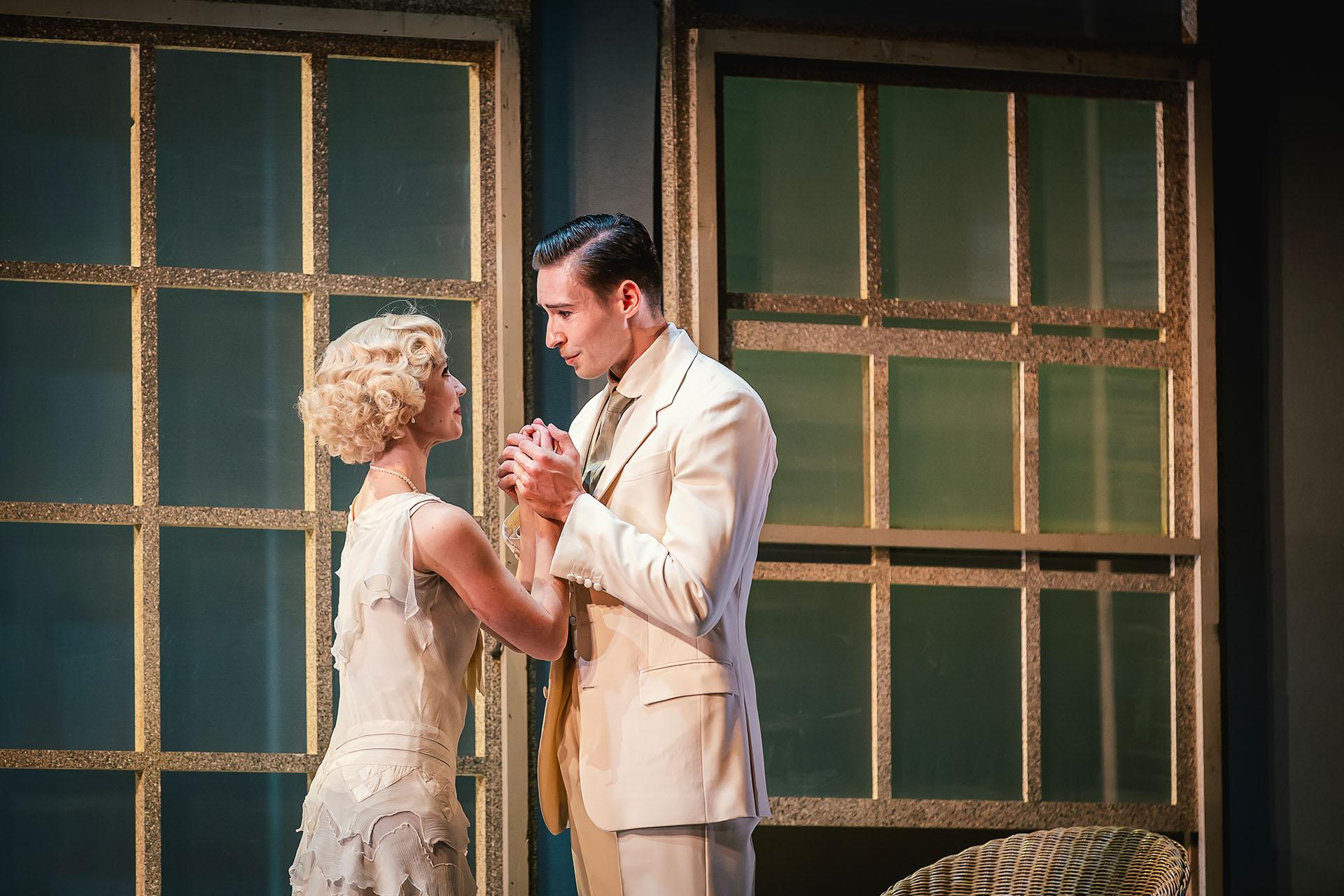 Two dancers dressed in smart white clothes gaze lovingly into one another's eyes whilst hold hands