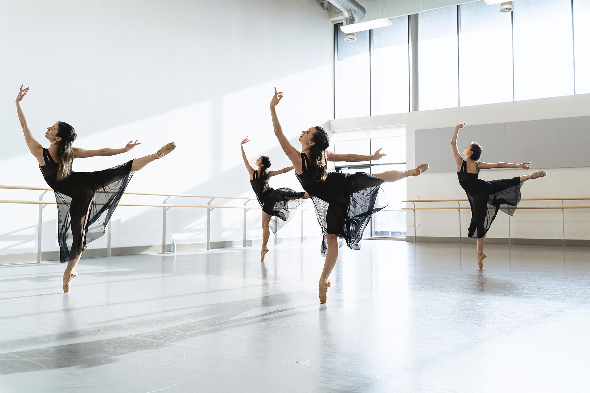 Four female dancers in black dresses in a long arabesque