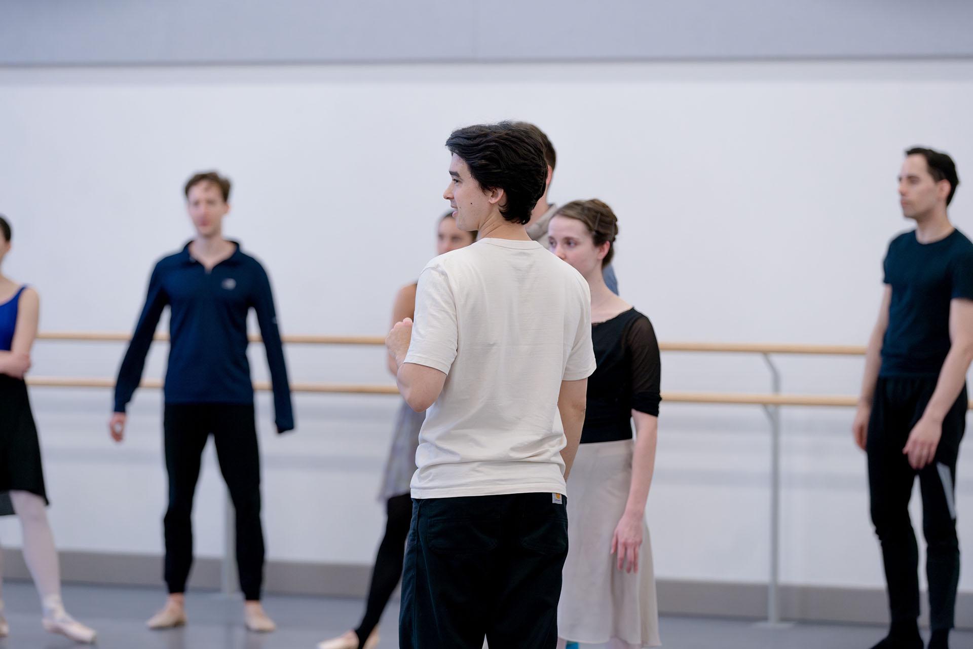 A choreographer stands in front of a group of dancers instructing them