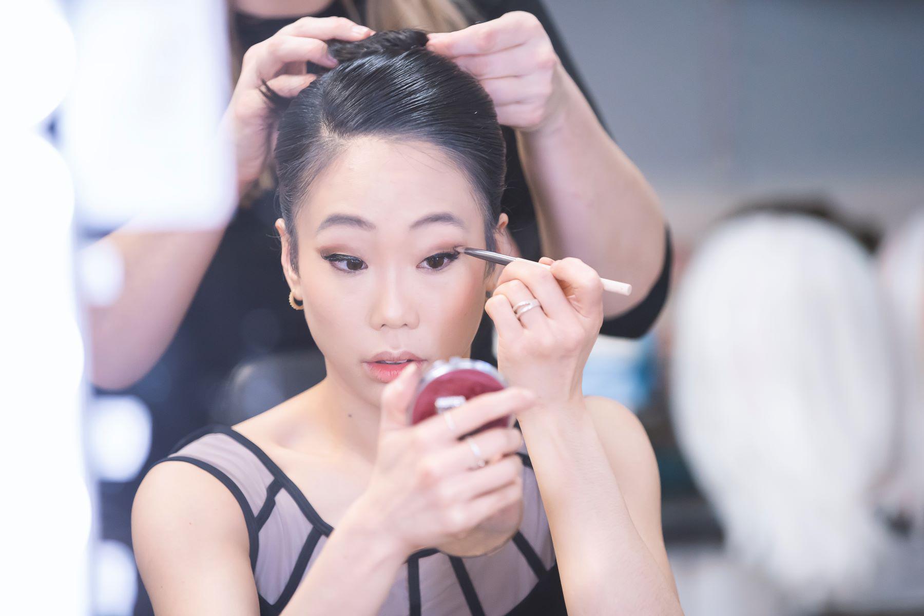 A female dancer applies mascara to her eyes.