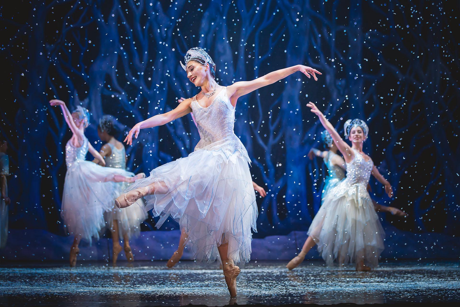 Women dressed in white, dancing as snowflakes during a snow fall on stage