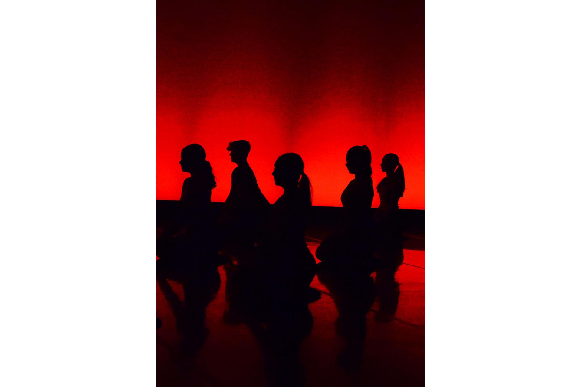 Silhouette of five people sat on their knees seen against a red illuminated background