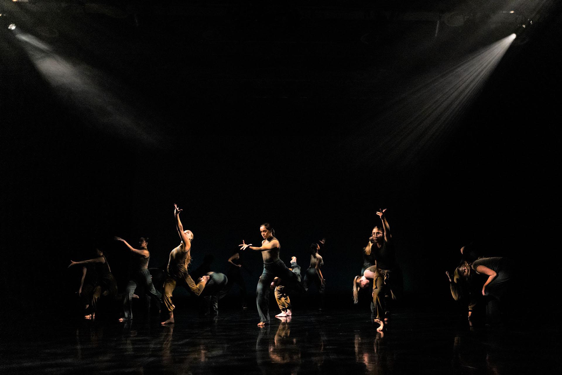 Group of dancers on stage performing against a black background