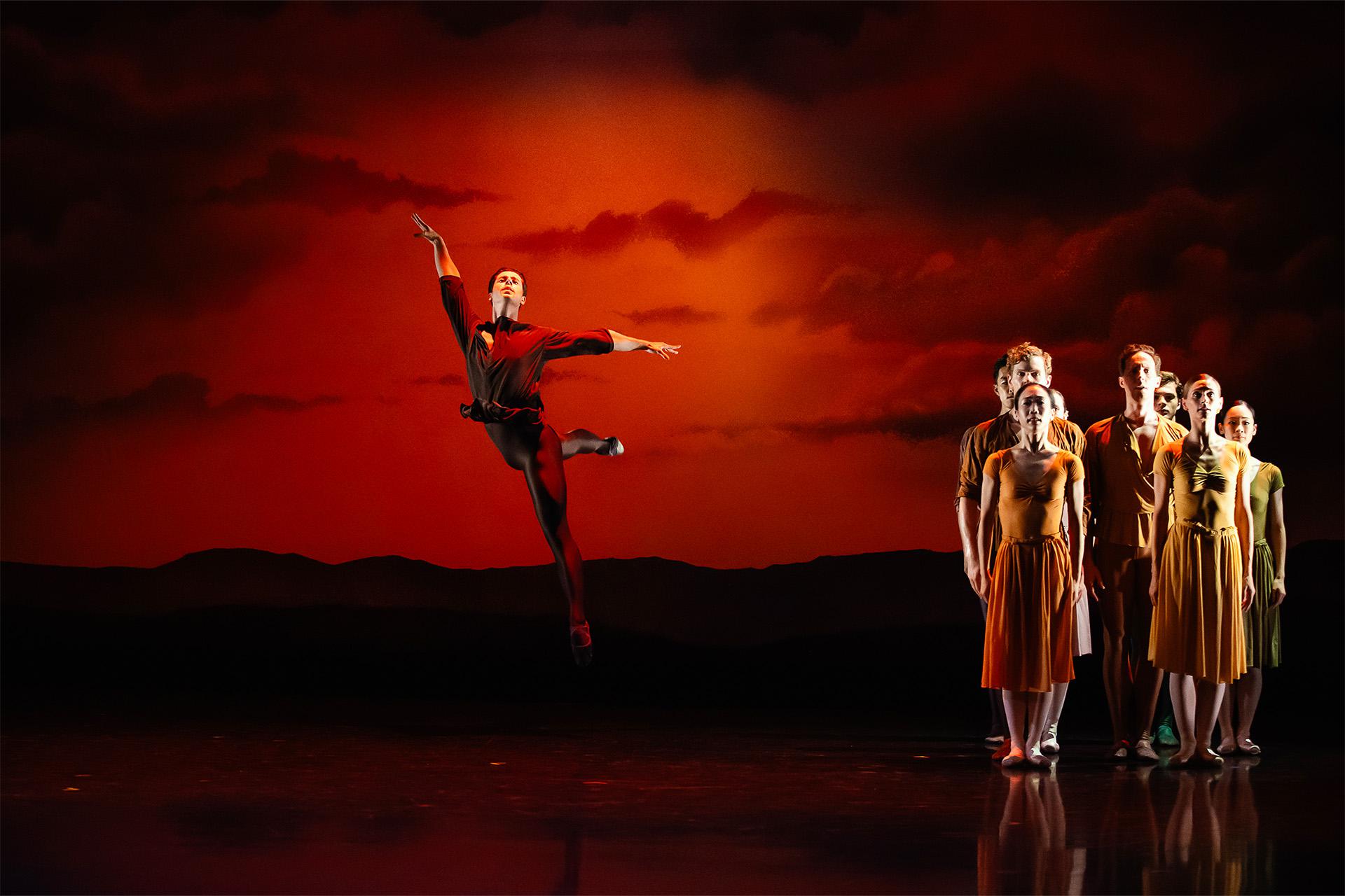 Dressed in red, a dancer leaps high against an orange sunset