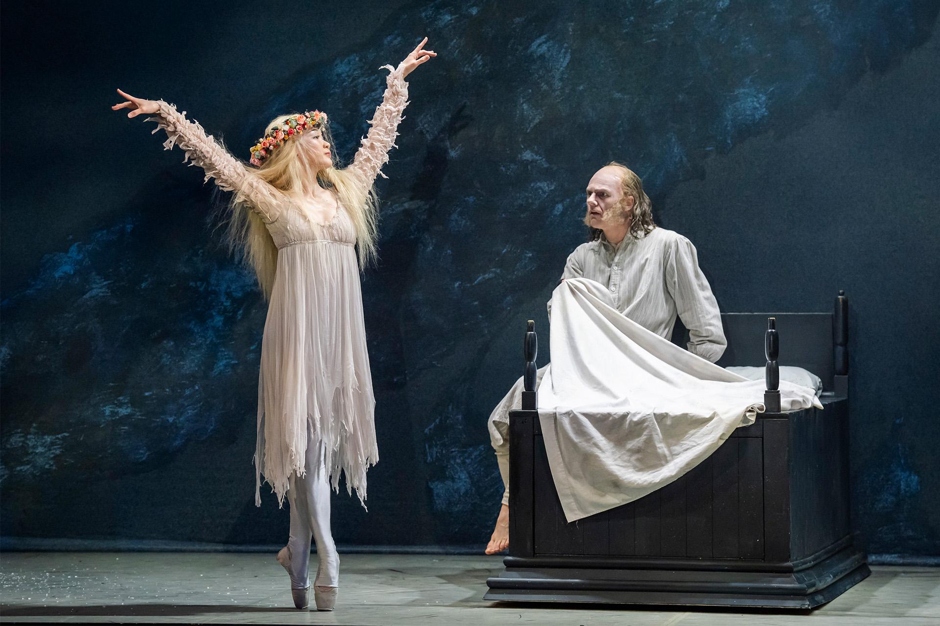 As Scrooge is abed the Ghost of Christmas Past poses in front of him, en pointe and arms raise above her head