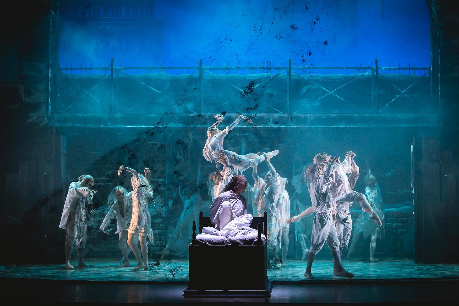 Scrooges sits up in his bed as wraiths dance behind him