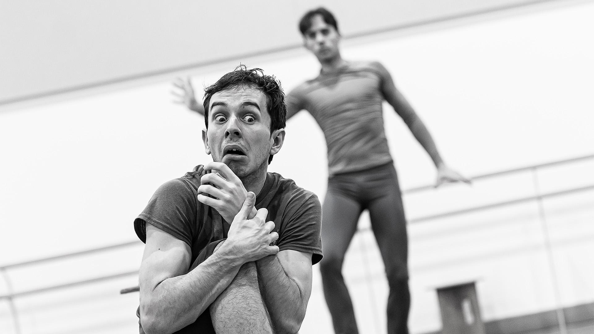 A dancer crouched down in fear with a dancer behind blurred in the background