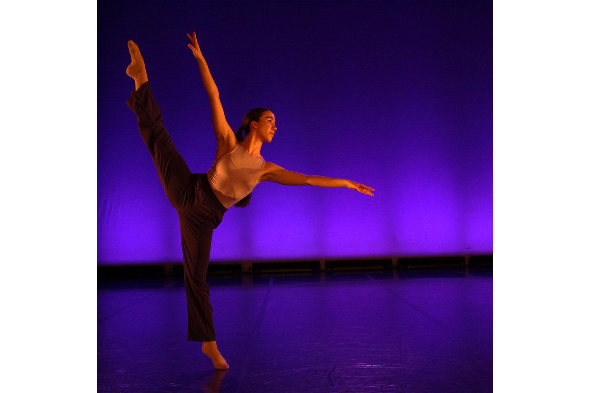 Dancer on one straight leg, the other raised, toes pointed and her arms wide