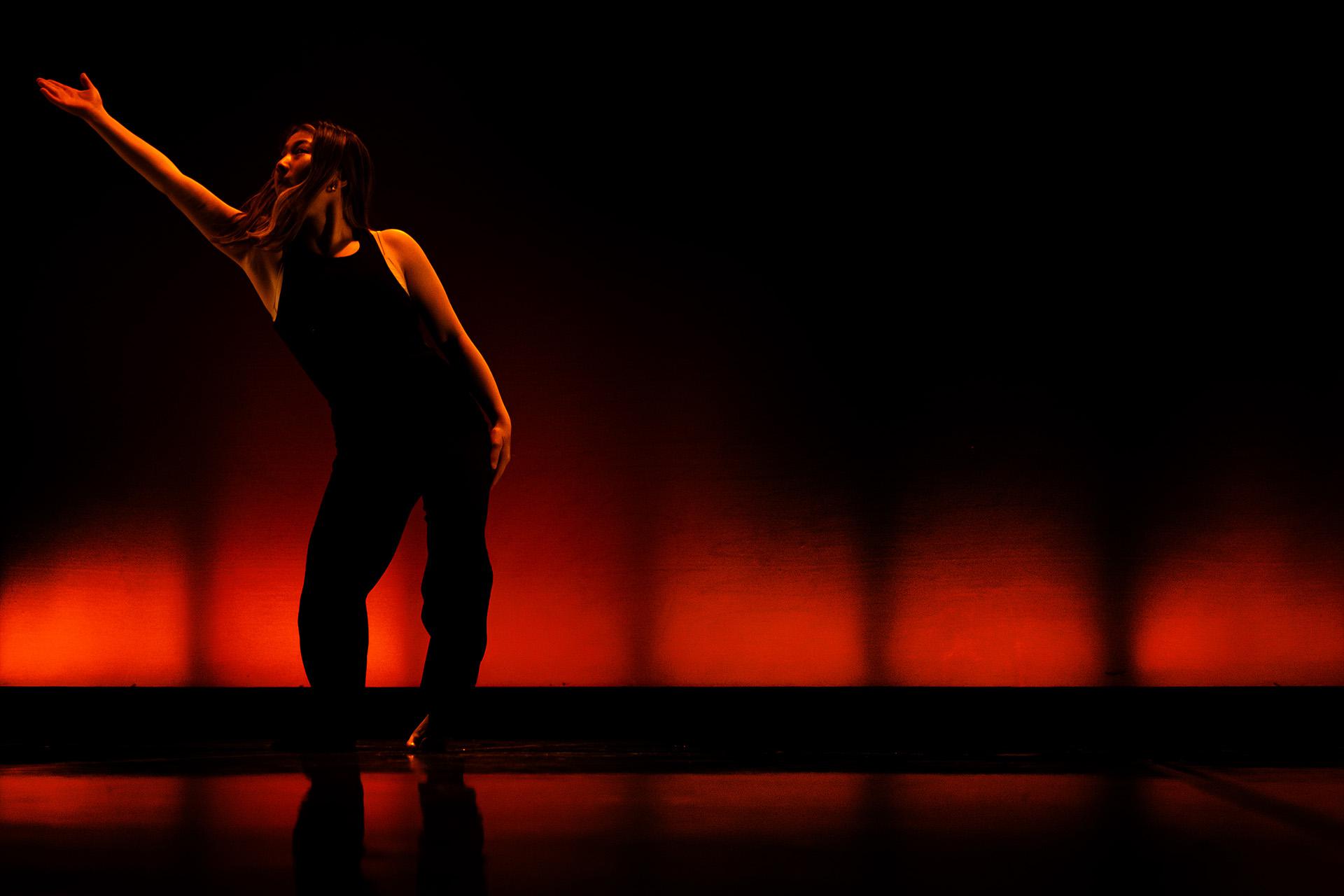 Dancer in dark with subtle red lighting, pases with one hand in the air
