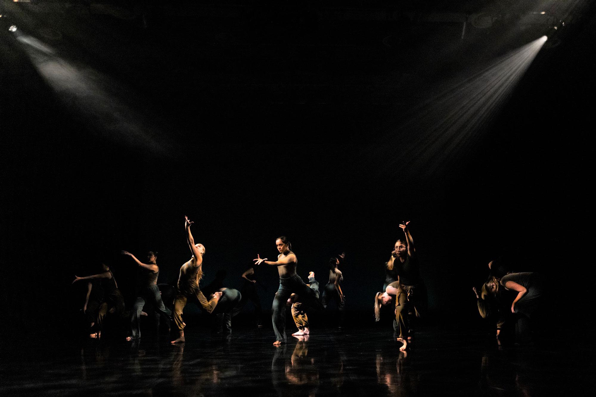A photo of a group of dancers in various dance positions against a black background with atmospheric white light