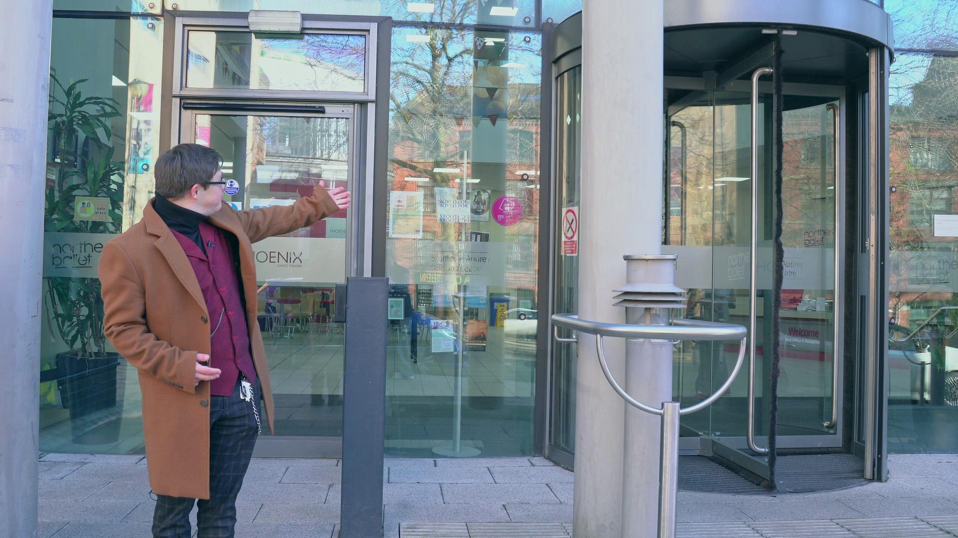 Man stood in front of the entrances to Northern Ballet, an accessible powered door and a revolving door