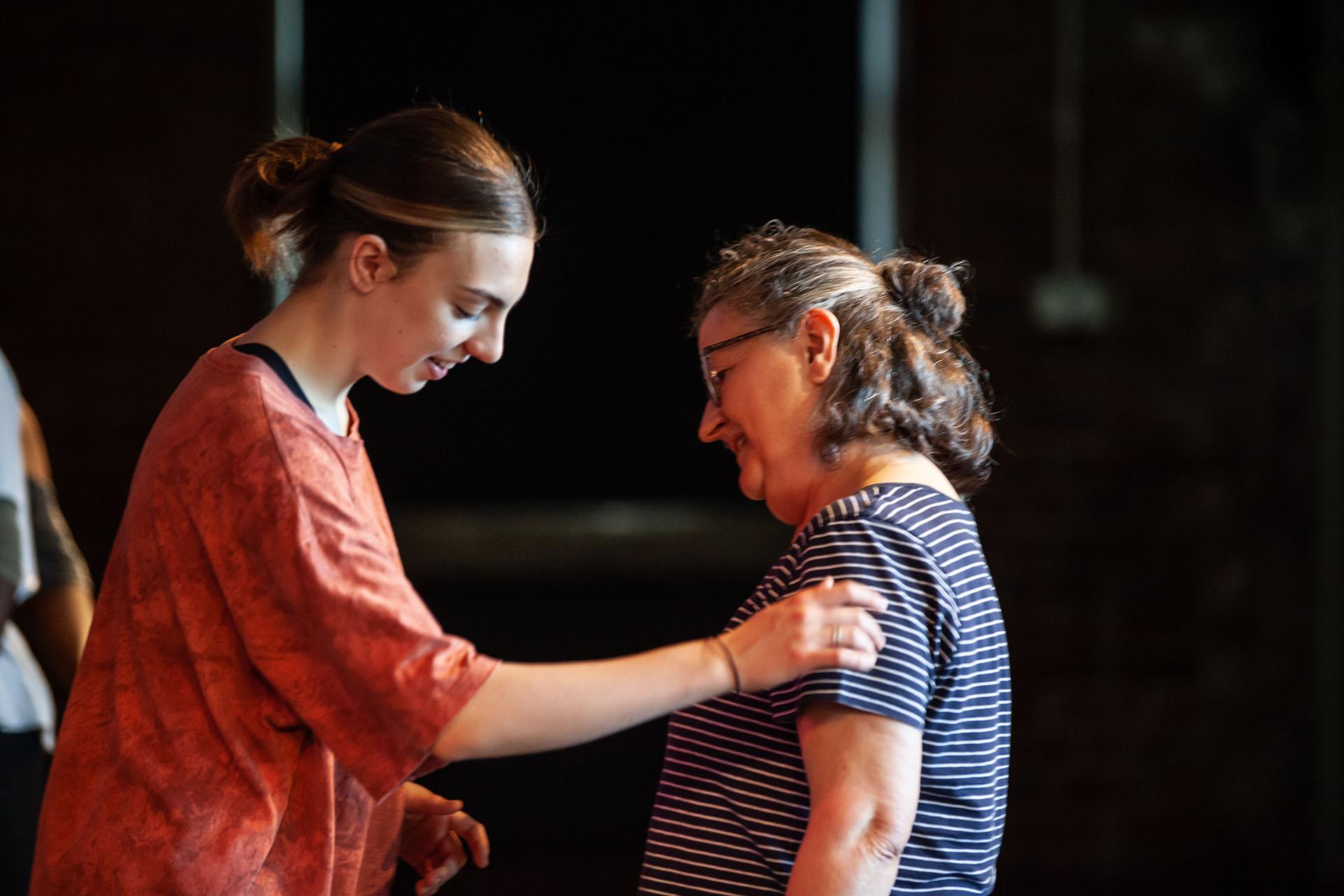 Woman with her eyes closed speaking with another, whose arm is guiding the former as they move to the correct position