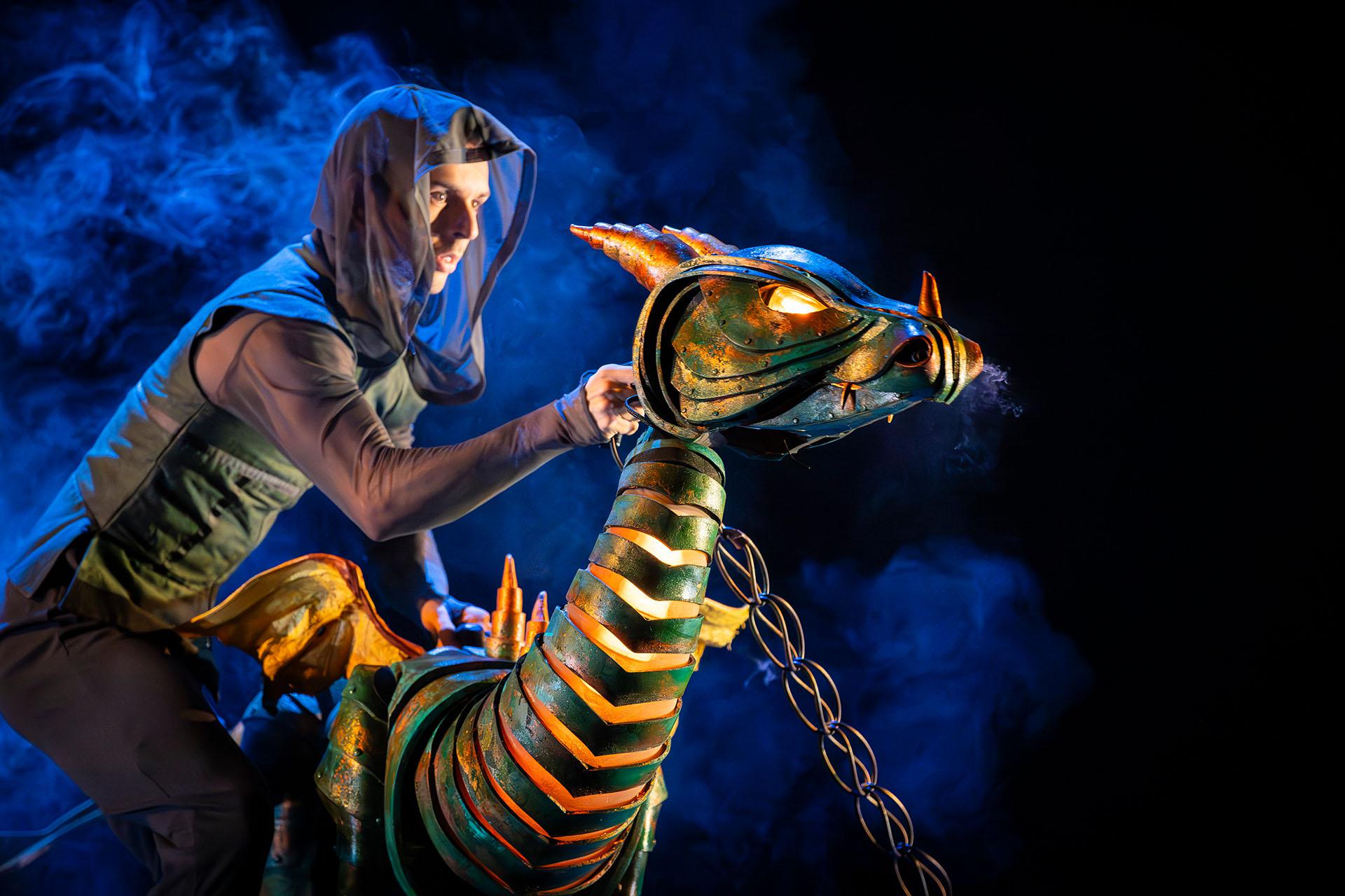 A young dragon, his eyes glowing and light visible through his scales; chained tied to his neck and a puppeteer posing him dramatically.