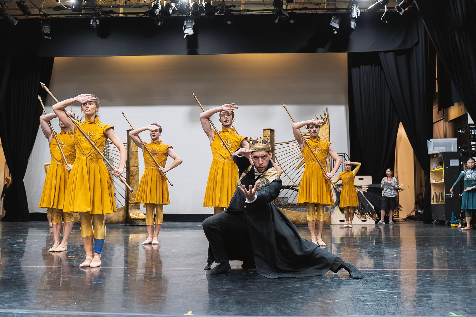 Army in yellow carrying pikes all salute as one, their monarch dressed in black in front of them