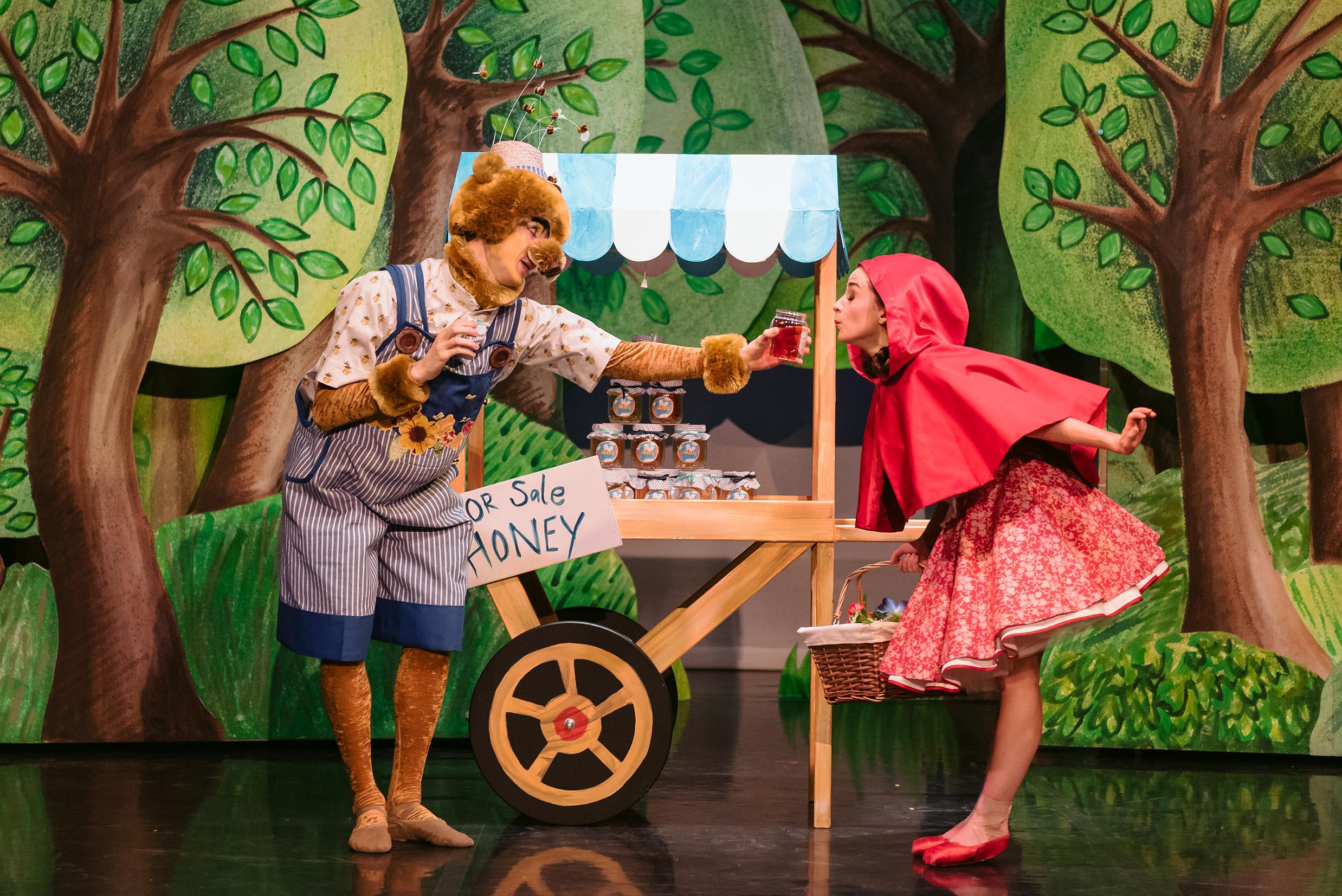 A dancer dressed as a bear offers honey to Little Red Riding Hood