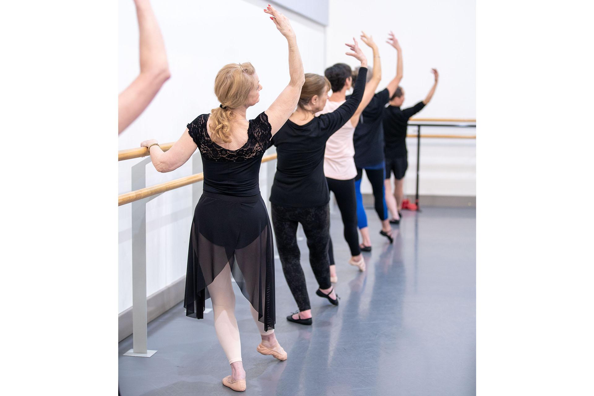 Dancers on the Over 55s class stand at the barre with one had resting on it and the other above their head
