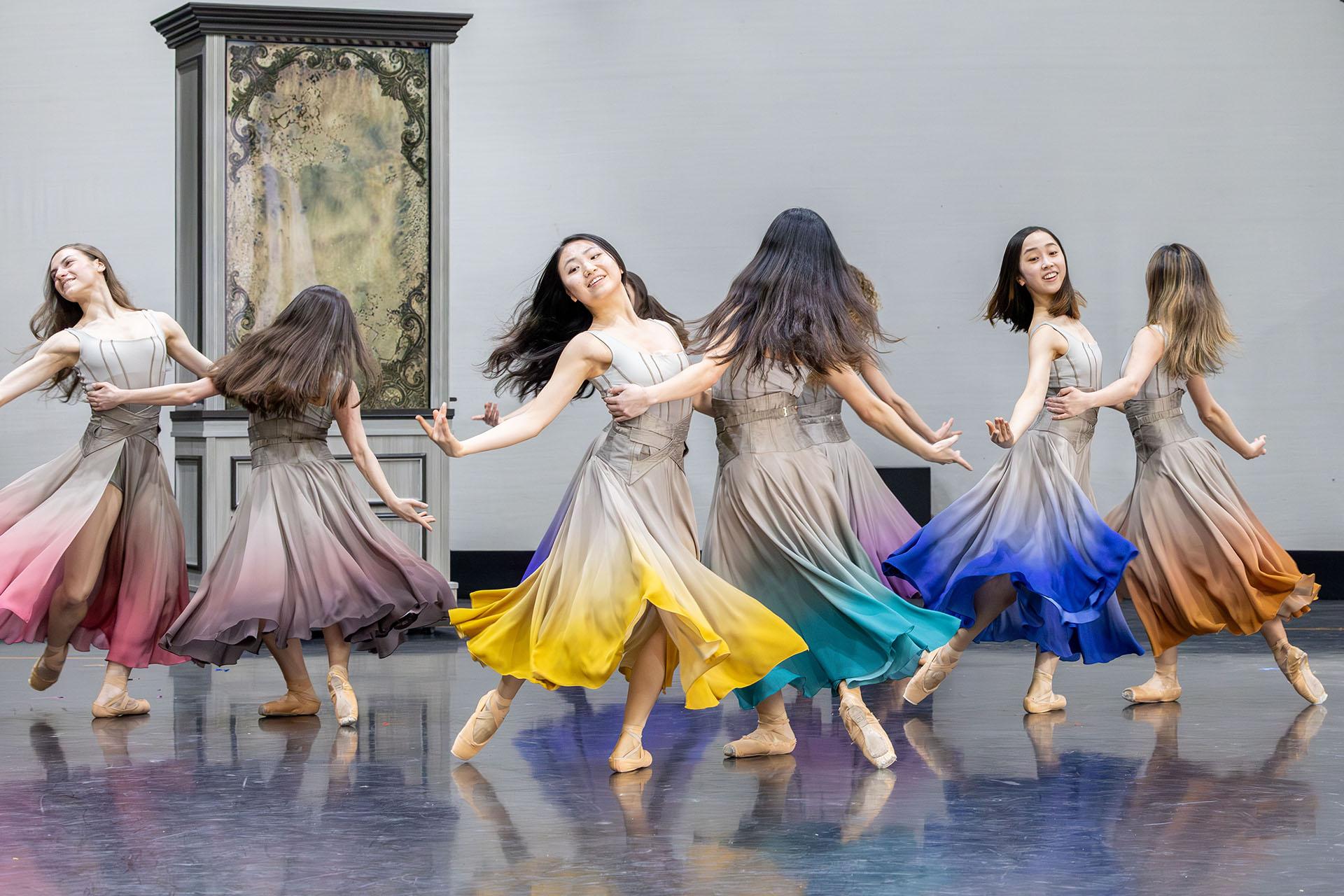 A goup of women dancing joyfully, all wearing similar dresses with a different colour skirt