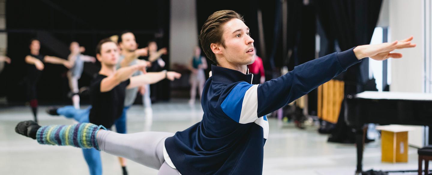 A Northern Ballet dancer, facing the right with their right arm stretched out and their left leg stretched behind them.