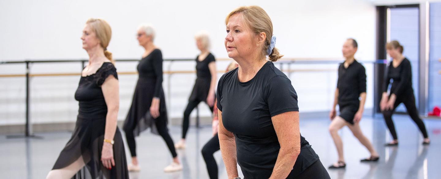 A cohort of participants on the Over 55s class standing one foot in front of the other, arms by their side or on the leading thigh