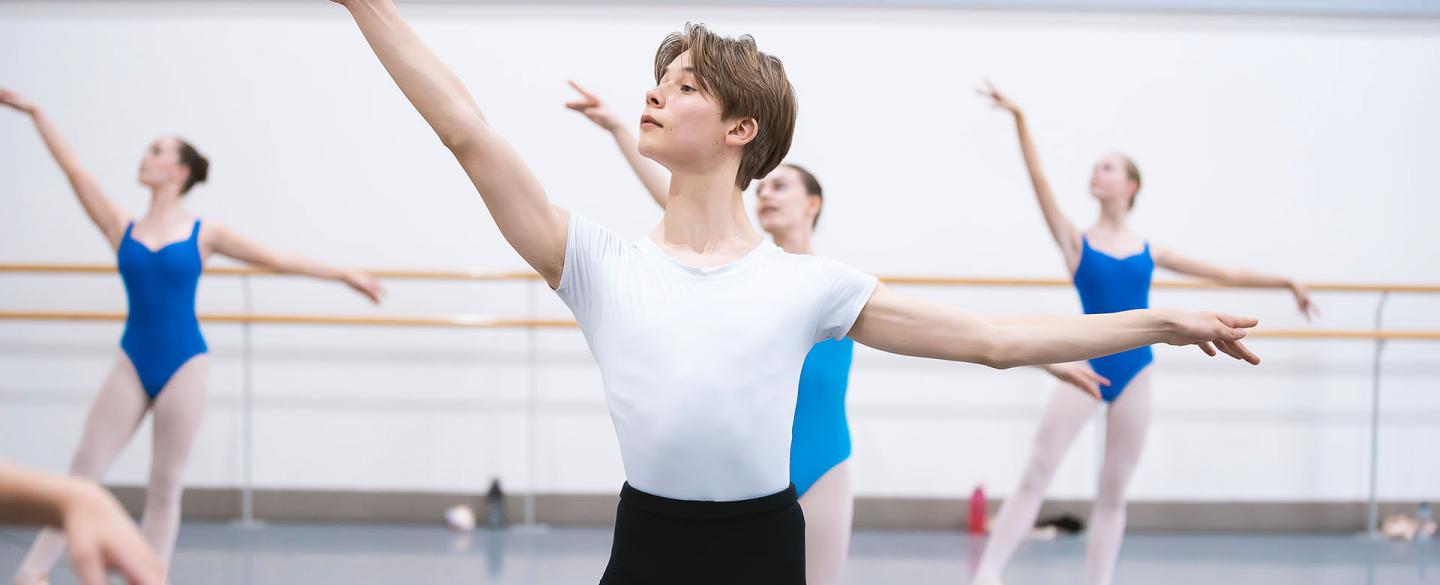 Male Centre for Advanced Training student in a white top and black trousers posing with his left arm our horizontally and his right raised slightly