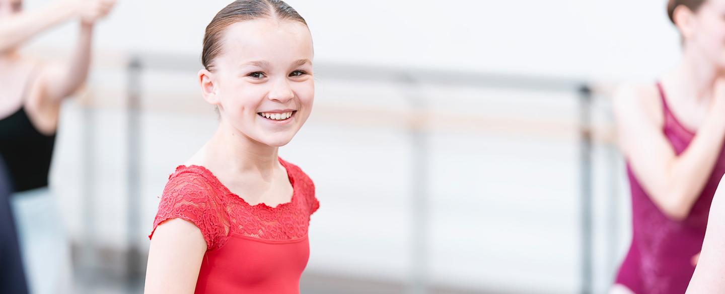 Young student in a red top standing in a studio smiles broadly direct to the camera