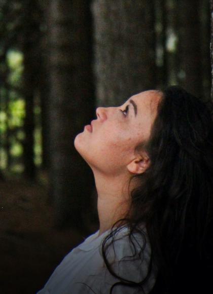 A woman stood in a tall forest looking upwards