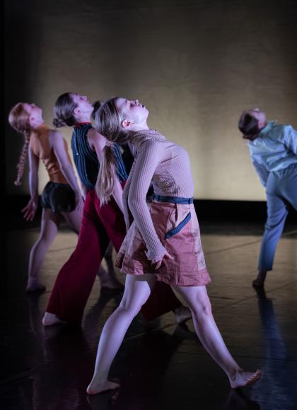 Dancers stepping forward on a stage with their heads leant back. 