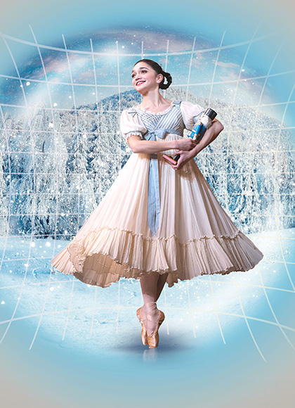 A dancer in Edwardian costume hold a Nutcracker doll in her arms, stands en pointe and smiles with childlike wonder