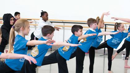 Group of you people practicing balancing on one leg with one leg stretched behind them and balanced from their bodies leaning forward.