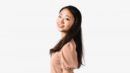 A headshot of a woman looking forward with dark brown hair and a peach coloured top