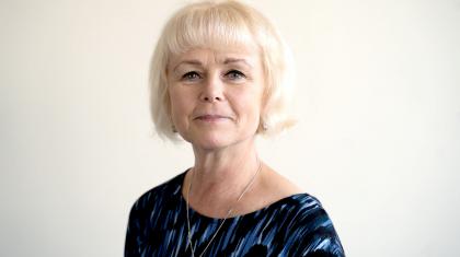 Woman with white hair smiling at the camera wearing a black and blue patterned shirt