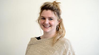 Woman smiling at the camera, she has long dark-blonde hair partly tied up and is wearing a cream coloured wool shawl