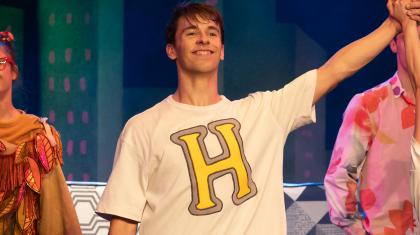 Hansel smiling broadly wearing a white T-shirt with his first initial emblazoned in yellow