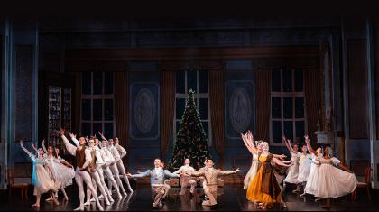 A party of dozens dressed in Regency attire all striking a pose, Christmas tree in the background