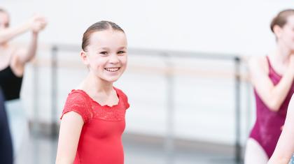 Young student in a red top standing in a studio smiles broadly direct to the camera