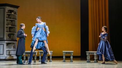 Anne Lister in a frock coat looks at Marianne, wearing a blue dress and lifted from the waist by her father as her mother looks on